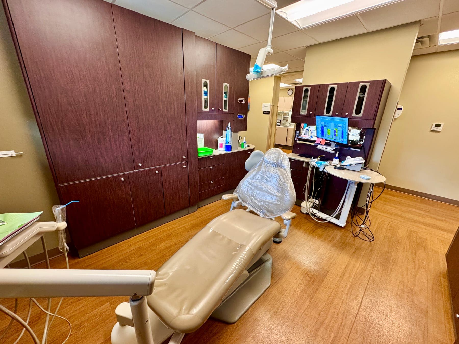 A dental treatment room with a reclined chair, cabinets and a monitor